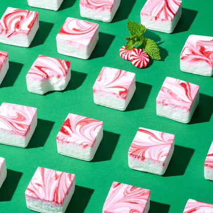 Marble-patterned pink and white marshmallows on a green background with peppermint candies and leaves.