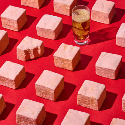 Square marshmallows on a red background with a glass of iced tea.